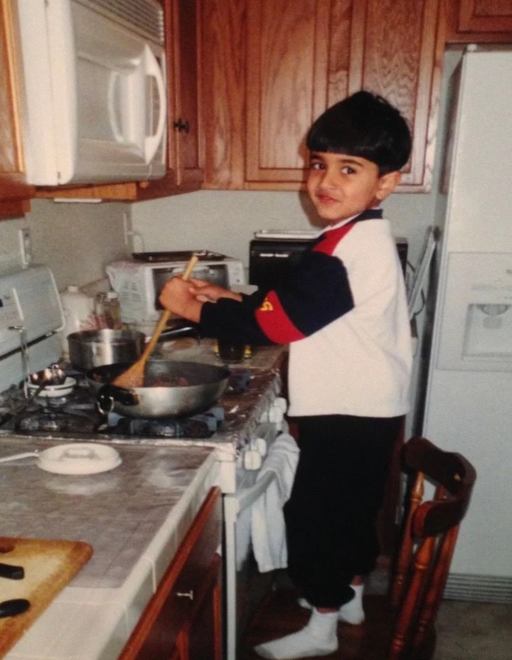 Standing on a kitchen chair as a child, stirring a pan on the stove.