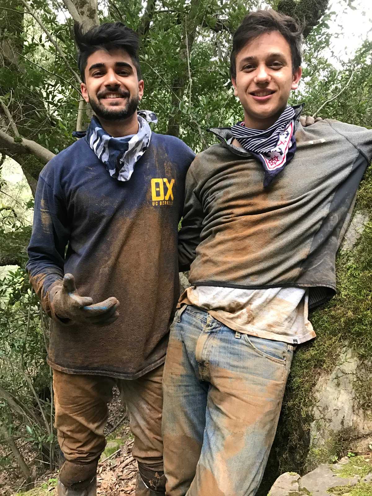 Two people in muddy clothes among trees.