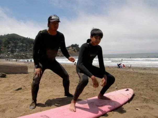 Practicing a surfing stance on a pink board on the beach with an instructor.