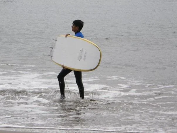 Carrying a white and yellow surfboard through shallow water.