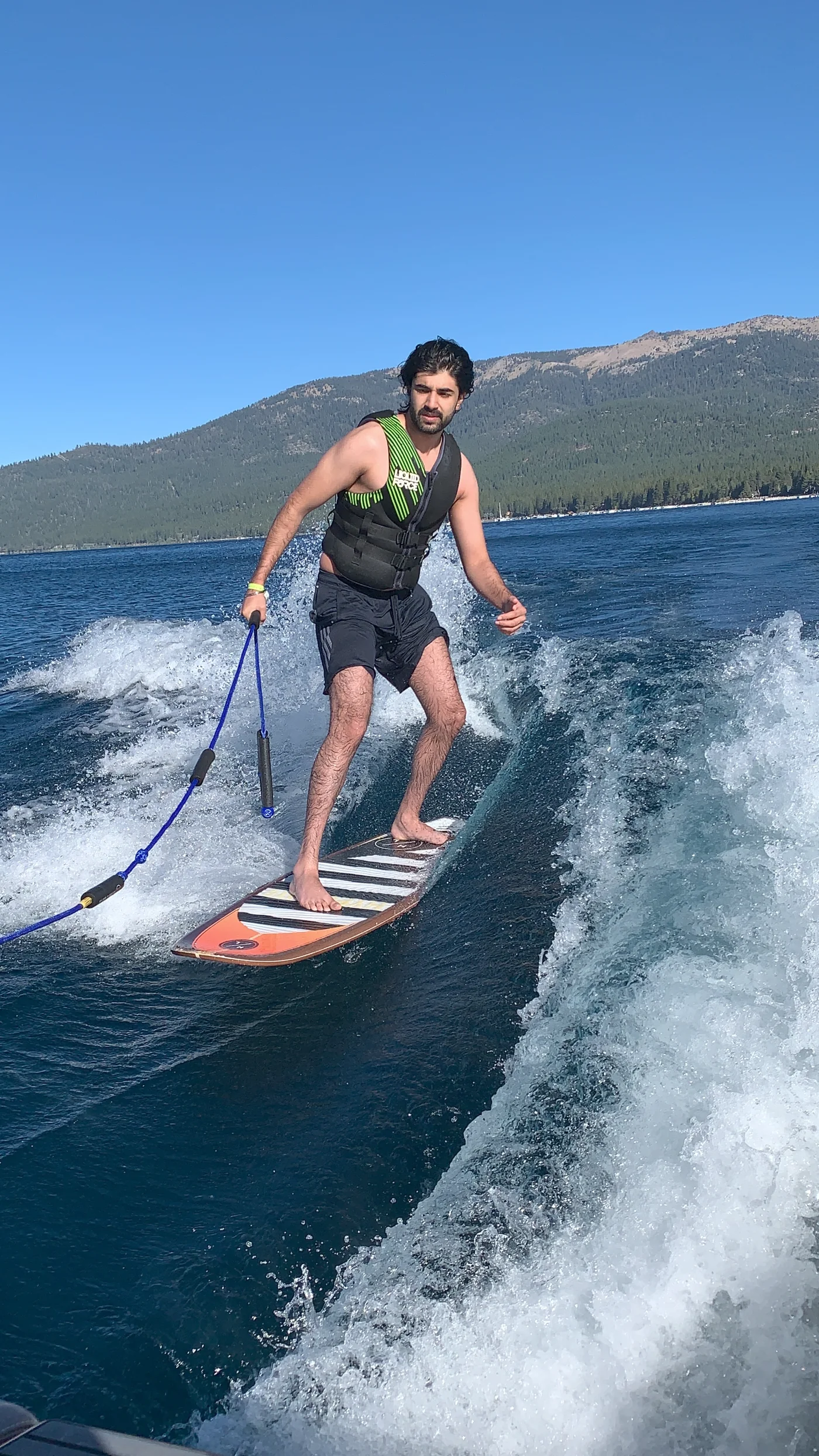 Wakesurfing barefoot behind a boat, holding a tow rope, with mountains across the lake.